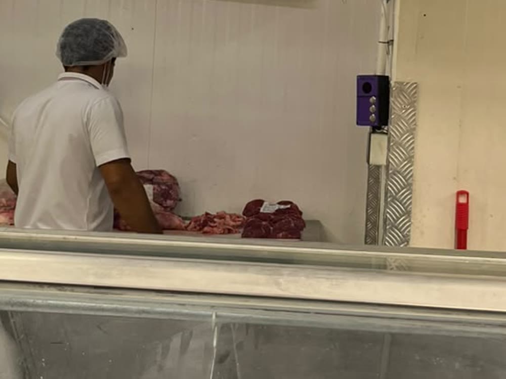 Açougueiro trabalhando na produção, com o dispositivo de controle roxo de três botões fixado na parede ao lado